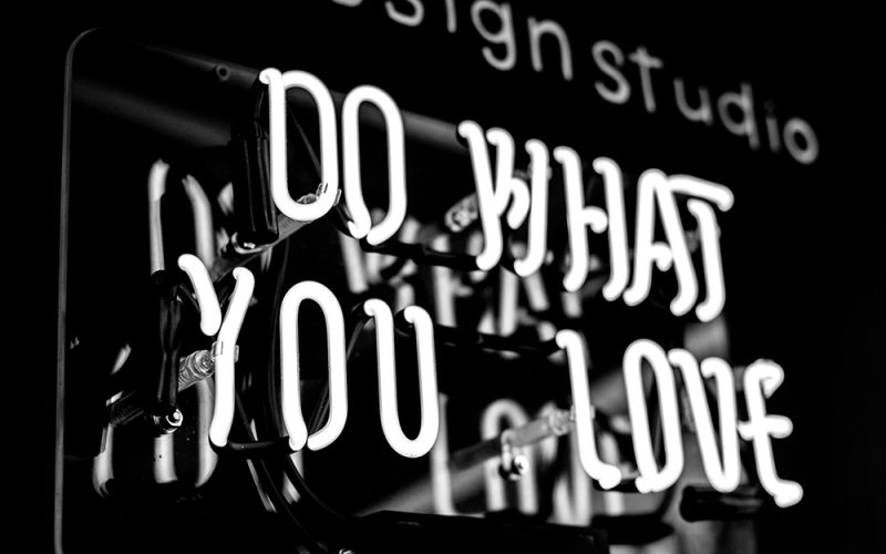 A black and white photo of a glowing neon sign reading DO WHAT YOU LOVE, with part of another design studio sign blurred in the background—perfect inspiration for HR onboarding spaces.